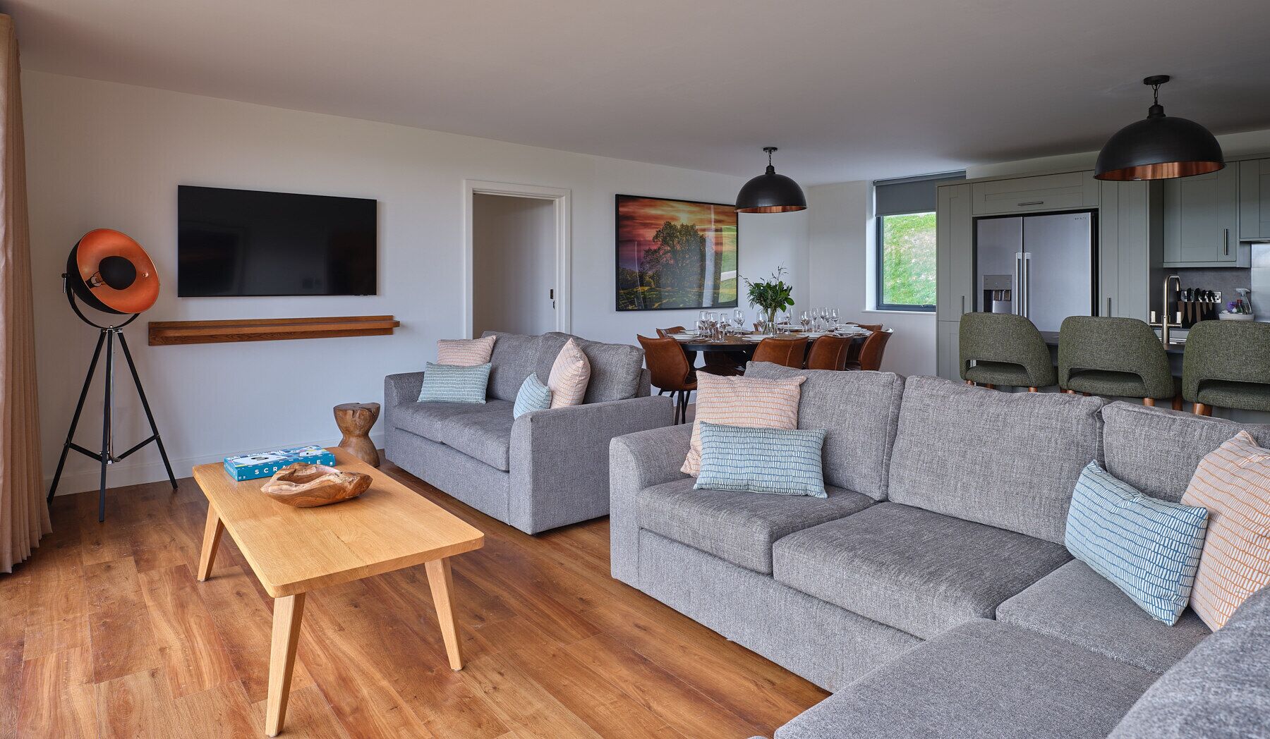 En moderne stue med grå sofaer, et træbord og et spiseområde med et bord dækket til fire personer.