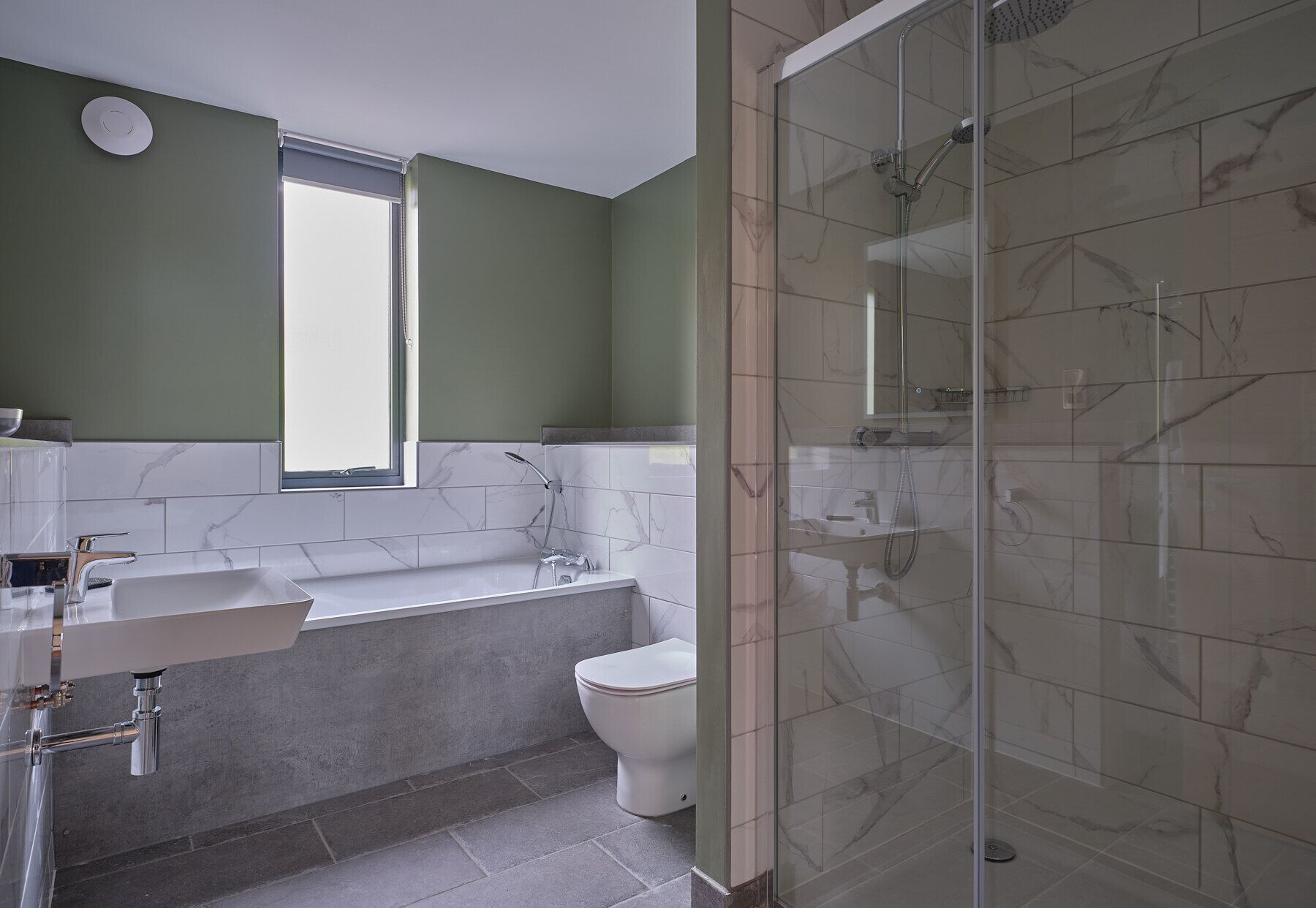 Ein modernes Badezimmer mit Badewanne, Toilette und einer in Glaswänden gefassten Dusche.
