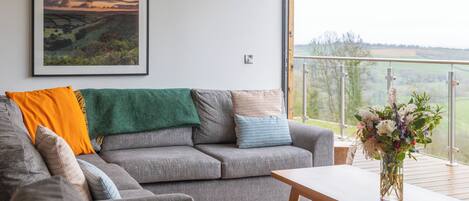 Een moderne woonkamer met een grijze bank, een houten salontafel en een lijstwerk met een landschapsdecoratie aan de muur.
