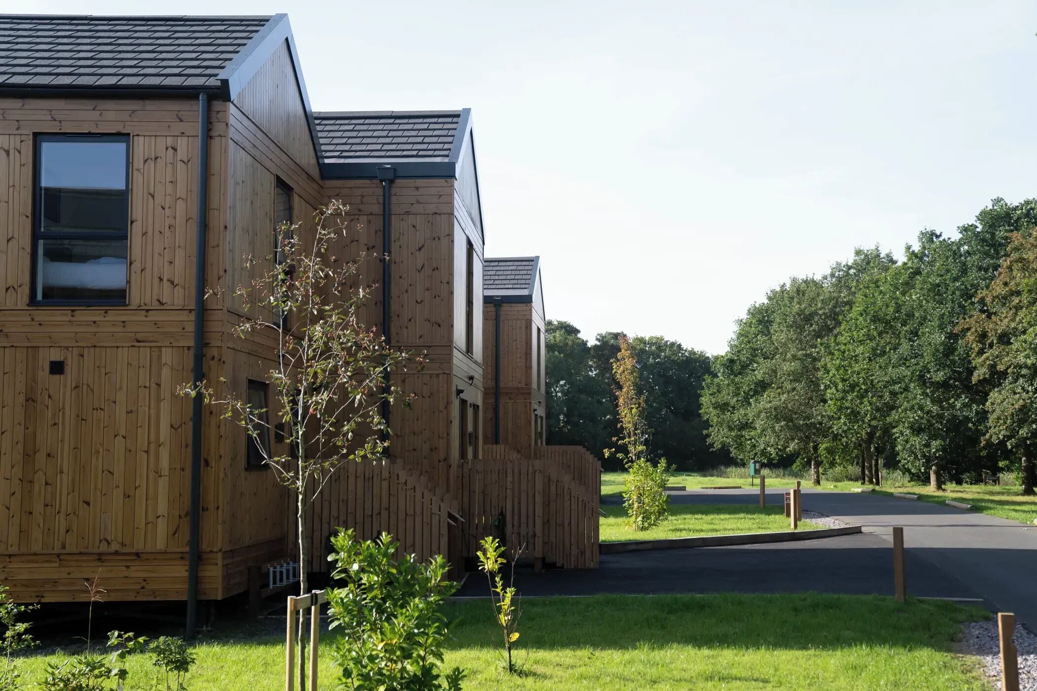 A modern wooden building with a sloped roof, surrounded by a well-maintained lawn and trees.
