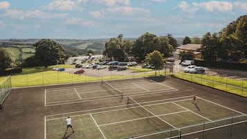 A tennis court with a net, surrounded by a parking area and buildings.