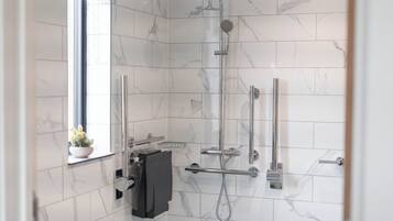 Een moderne badkamer met witte marmertegeltjes, een douchecabine van glas, een handdouche, een handdoekrek en een potplant.