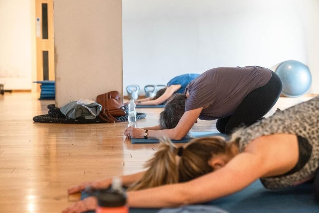 A group of people in a gym setting, engaged in stretching exercises on mats.