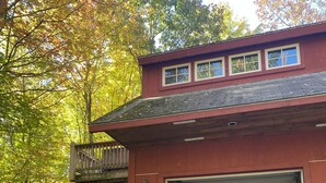 A red building with a garage door open, surrounded by trees with autumn leaves. - Lake & Mount Sunapee Apartment Getaway (Newbury)