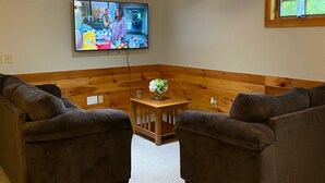 A living room with a ceiling fan, a television mounted on the wall, a wooden accent wall, and two brown sofas. - Lake & Mount Sunapee Apartment Getaway (Newbury)