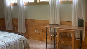 A room with a bed, a small wooden table, and a window with curtains. - Lake & Mount Sunapee Apartment Getaway (Newbury)