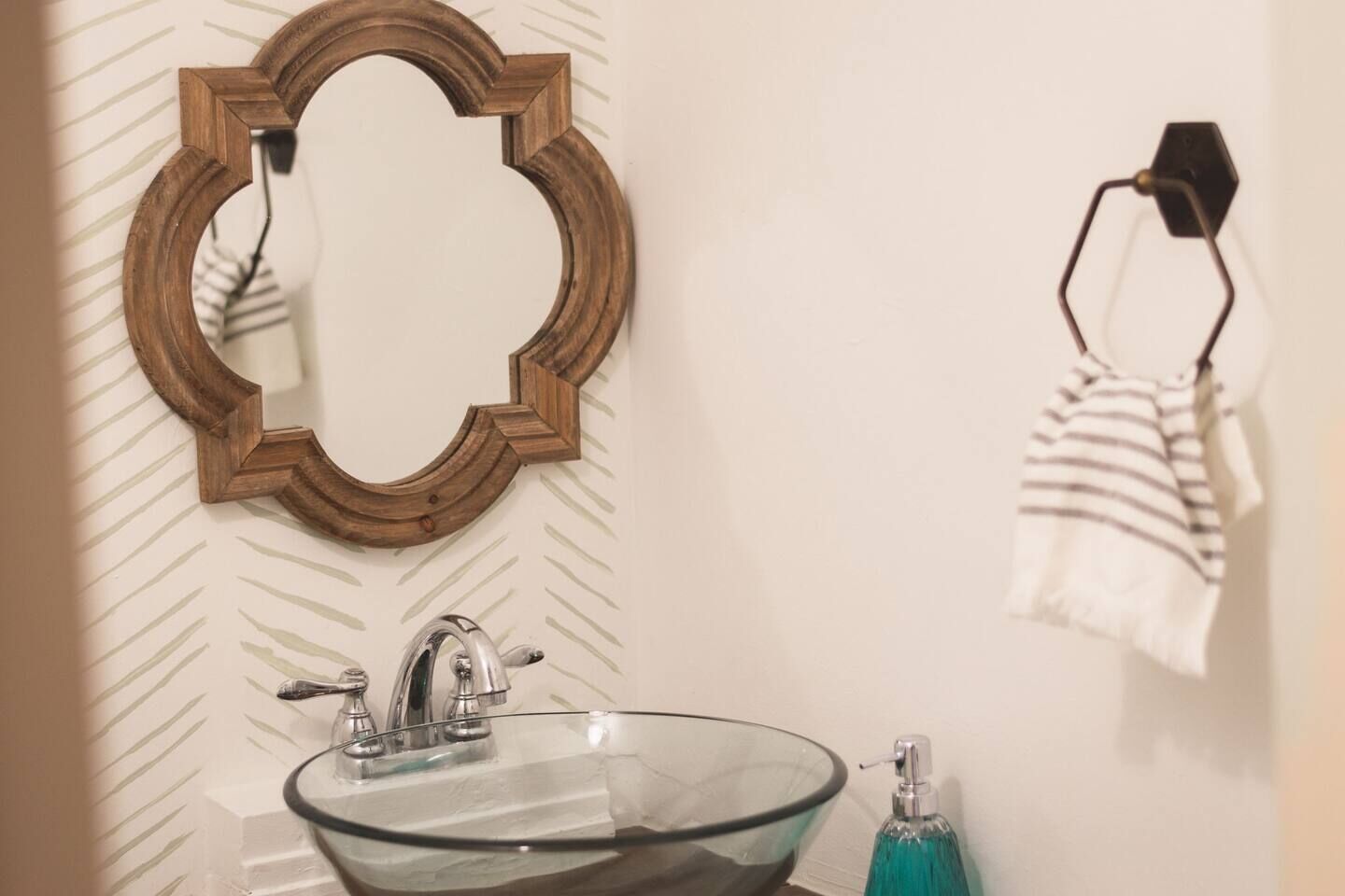 Une salle de bain avec un lavabo en verre, un miroir à cadre en bois et une serviette à rayures accrochée à un crochet.