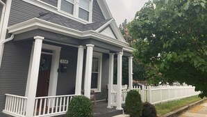 A two-story house with a porch, white columns, and a white picket fence. - That Corner Lot-Charming Downtown Home w/Side Yard (Troy)