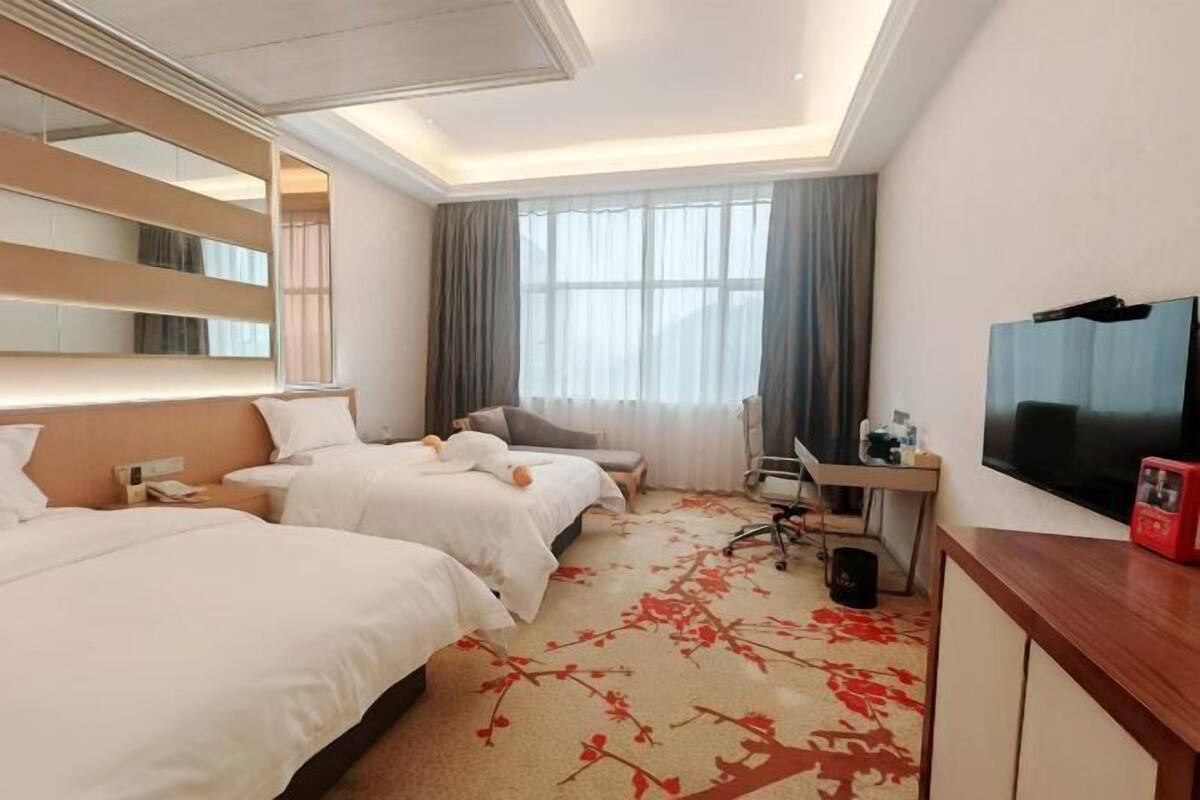 Habitación de hotel con dos camas, un escritorio, televisor y un ventanal grande con cortinas.