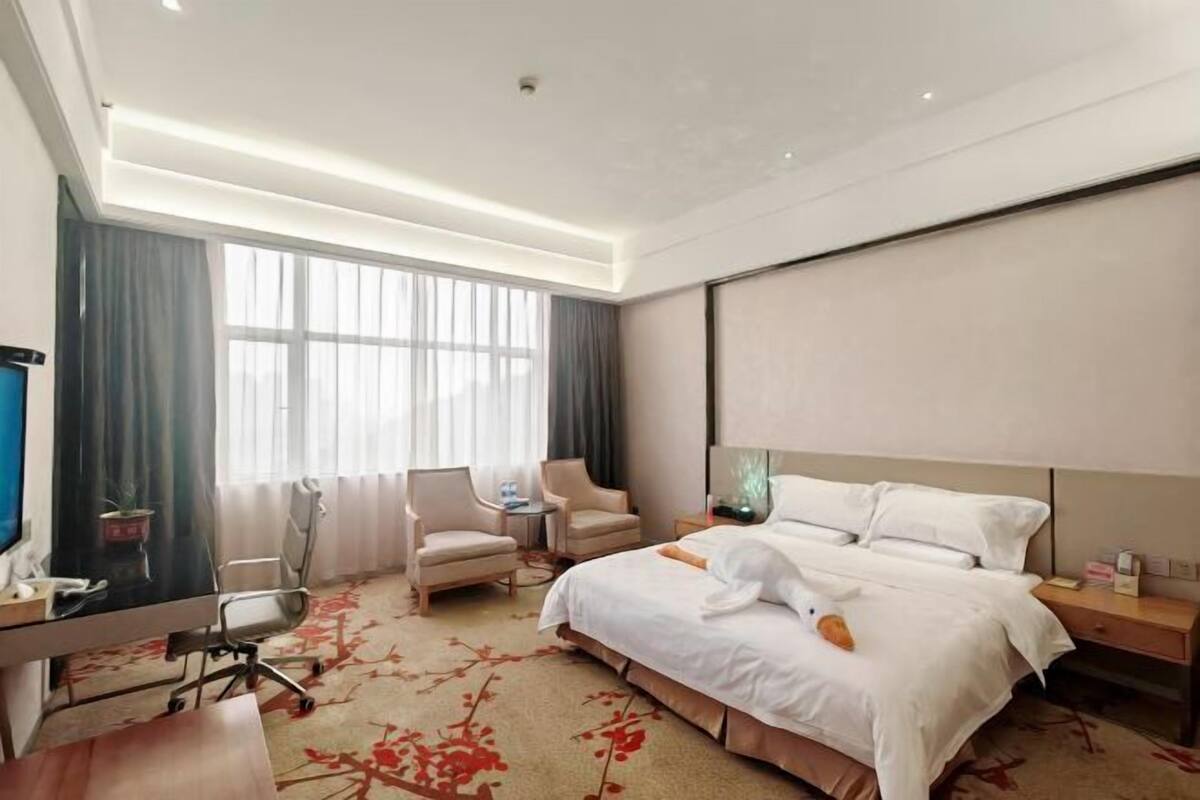 Una habitación de hotel con una cama grande, un escritorio con silla, televisión y ventana con cortinas.