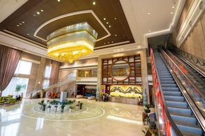 Eine Hotelhalle mit einer zentralen Fontäne, Rolltreppen und einem modernen Kronleuchter.