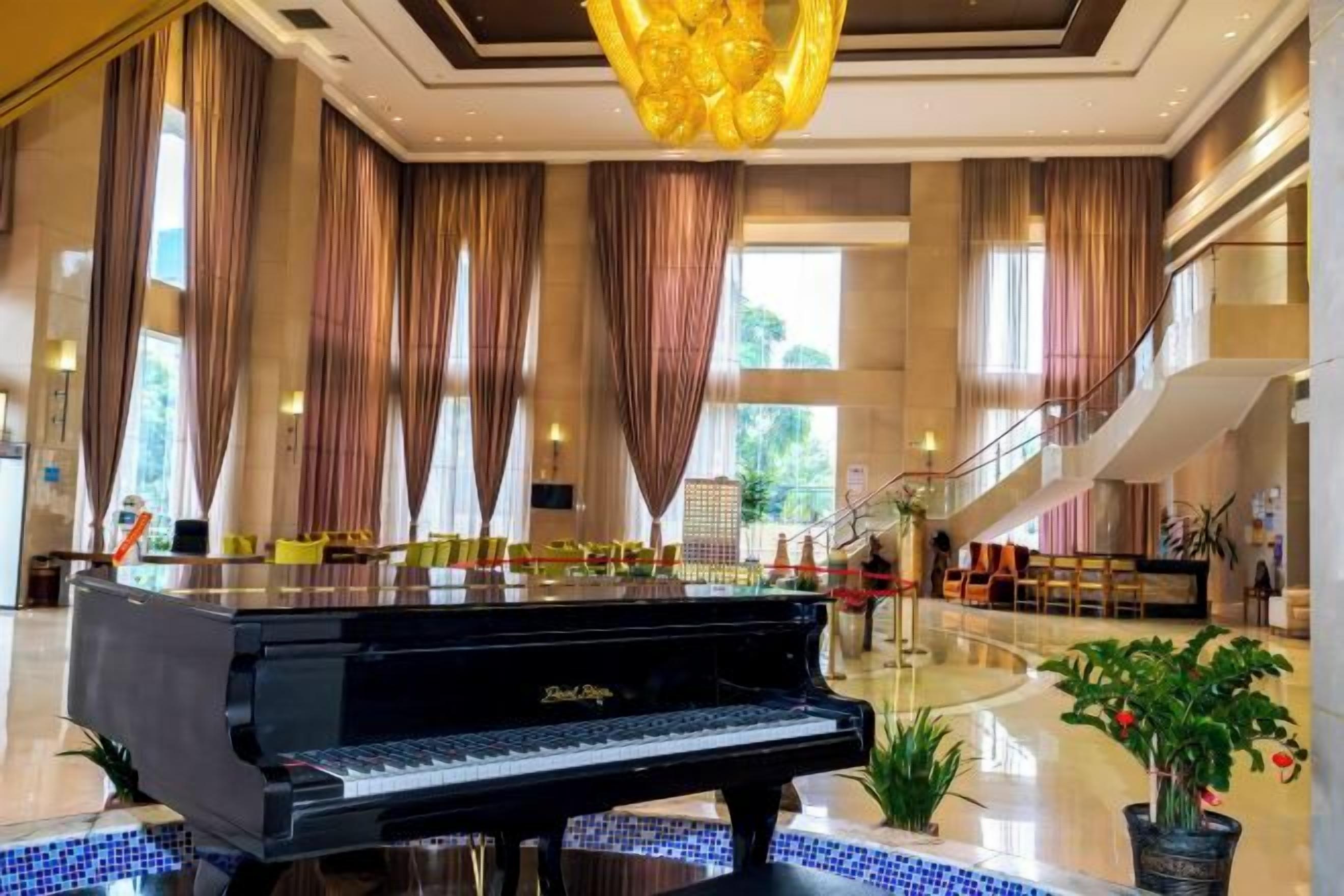 Un piano de cola en un vestíbulo amplio con techo alto, ventanas grandes y una escalera.
