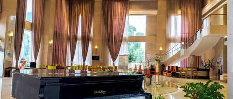 Un piano de cola en un vestíbulo amplio con techo alto, ventanas grandes y una escalera.