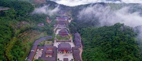 A traditional building complex with multiple structures, surrounded by lush greenery and mountains.