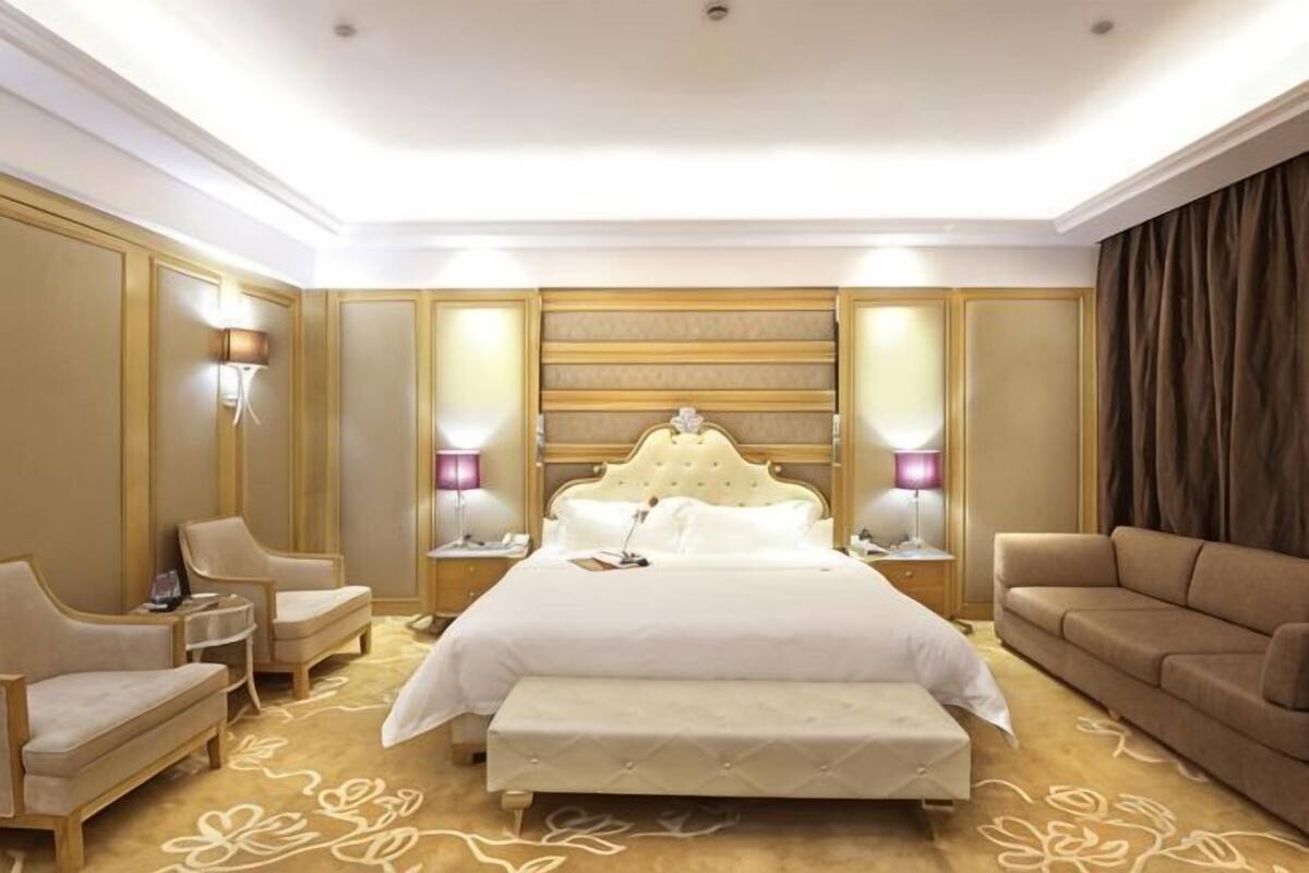 Una habitación de hotel con una cama grande, dos mesitas de noche, un sofá y suelo alfombrado.