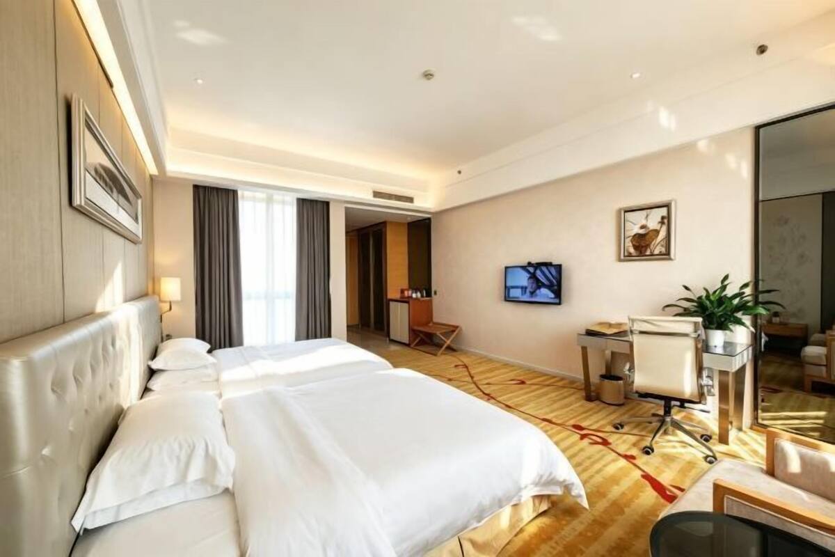 Una habitación de hotel con una cama grande, un escritorio, un televisor y un espejo.
