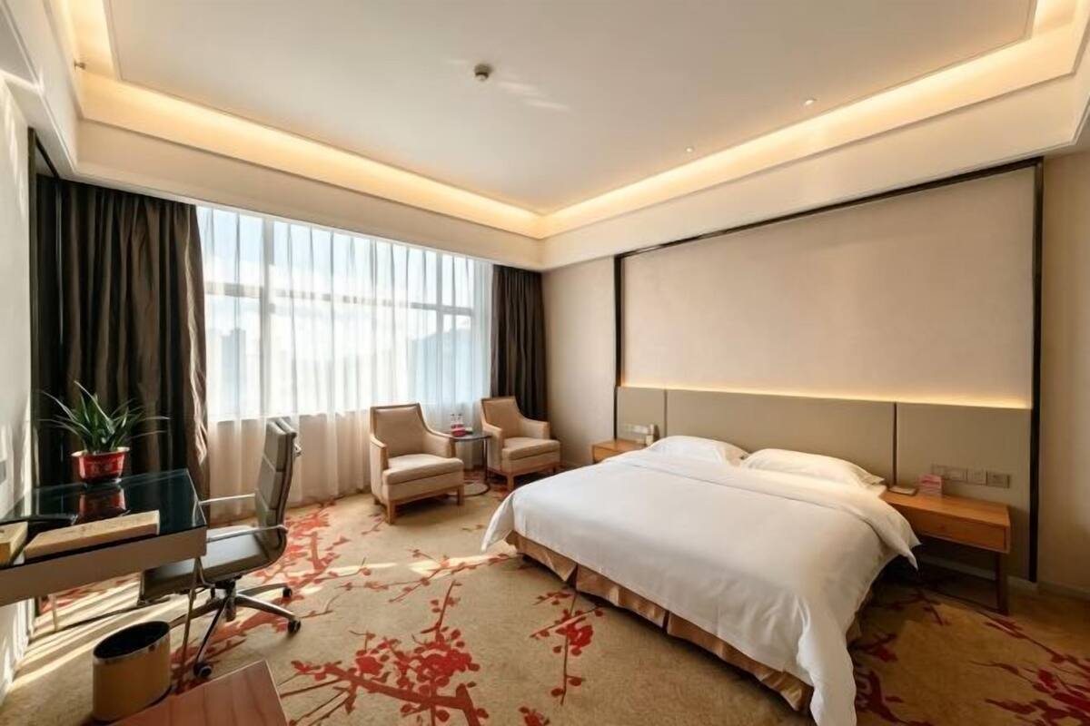 Una habitación de hotel con una cama, dos sillones, un escritorio y un ventanal grande.