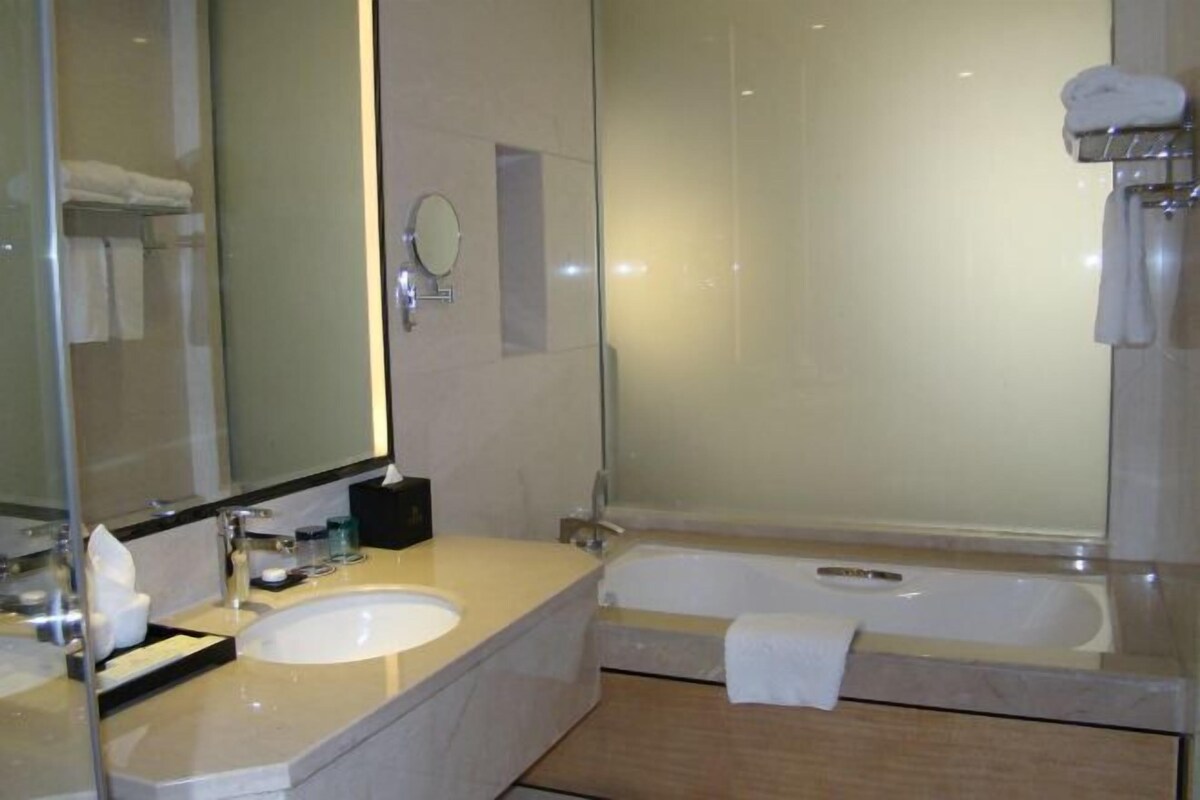 A modern bathroom with a large mirror, two sinks, a bathtub, and a shower.