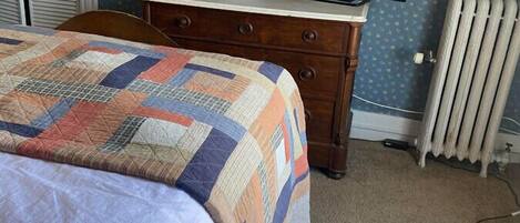 A bedroom with a bed, dresser, television, and radiator.