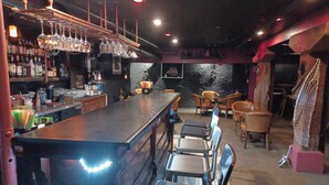 Zona de bar con una barra larga, varios taburetes y un soporte de copas de vino montado en la pared.