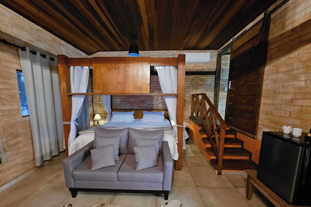 Um quarto aconchegante com uma cama, um sofá, uma escada de madeira e uma TV em um suporte.