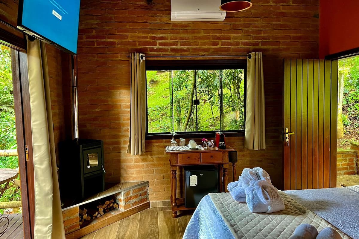 Um quarto acolhedor com uma cama, uma mesinha com chaleira, uma TV e uma janela com cortinas.