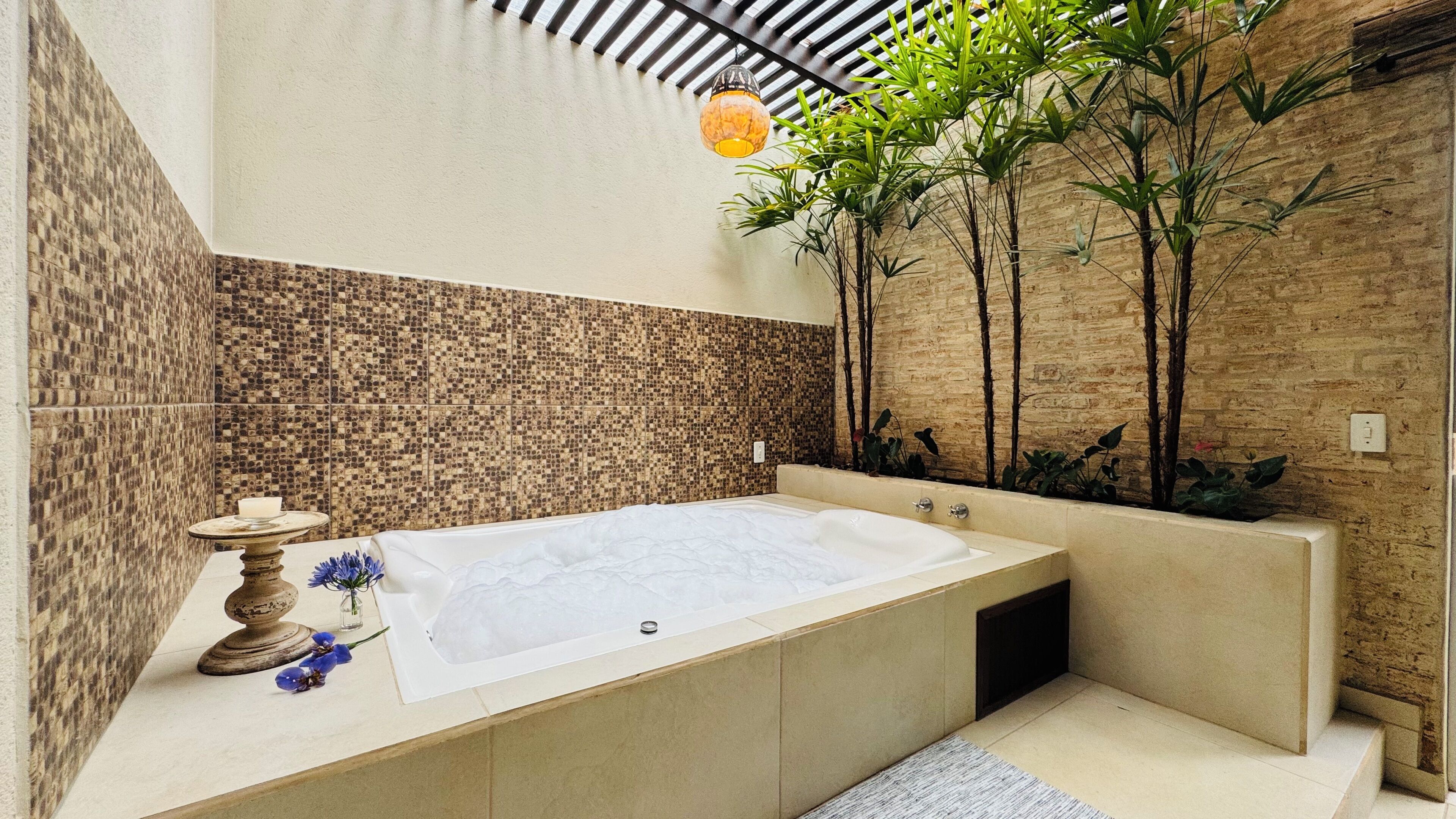 Un baño moderno con una bañera grande, paredes de mosaico y plantas de interior.
