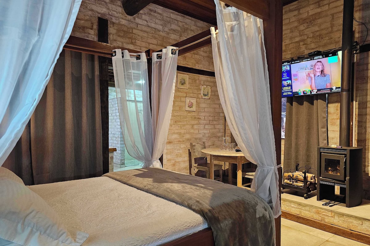 Quarto com cama, cortinas, televisão e lareira.