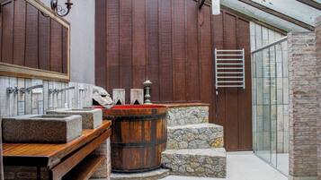 A bathroom with a wooden bathtub, a stone sink, and a glass shower enclosure.