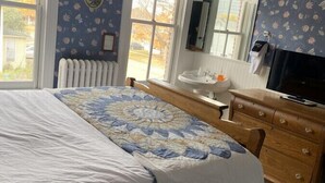 A bedroom with a large bed, a dresser, a television, and a window with curtains.