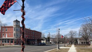 A street with a red and black checkered flag on a pole, a brick building with a clock tower, and a clear blue sky.