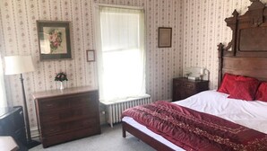 A bedroom with a wooden bed, a dresser, a radiator, and a window with curtains. - AH #18 · AH #18 King/Jacuzzi Suite/Fridge/Micro (Wabasha)