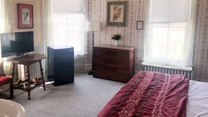 A bedroom with a bed, dresser, TV, and a radiator. - AH #18 · AH #18 King/Jacuzzi Suite/Fridge/Micro (Wabasha)