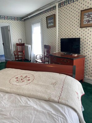 A bedroom with a bed, two chairs, a dresser, a television, and patterned wallpaper. - AH #34 · AH #34 Queen Suite w/Jacuzzi/SS/Fridge/Micro (Wabasha)