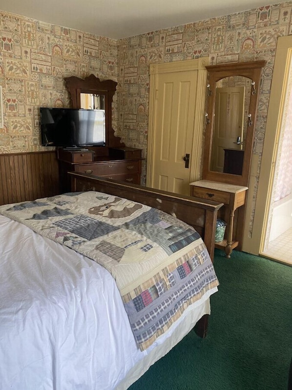 A bedroom with a bed, dresser, television, and a mirror.
