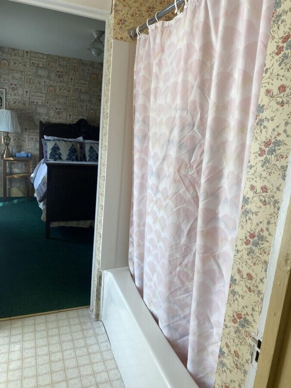 Un baño con cortina de ducha, una cama con colcha estampada y una pared con diseño de papel tapiz floral.