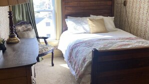 A bedroom with a wooden bed, a nightstand, a lamp, a chair, and a window with curtains.