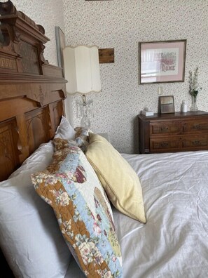 A bedroom with a wooden headboard, a floral-patterned quilt, a cream-colored pillow, a bedside table with a lamp, and a framed picture on the wall. - AH #8 · AH #8 Queen Suite w/Tub/Shower (Wabasha)