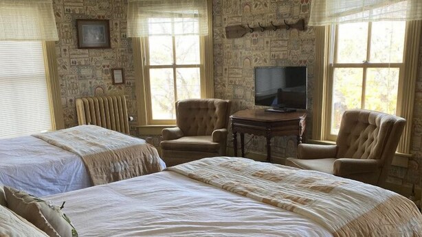 A hotel room with two large beds, a television, and a stone-patterned wall. - AH #36 · AH #36  Full x 2 w/Shower/Fridge/Micro (Wabasha)
