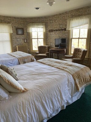 Quarto de hotel com duas camas grandes, televisão e parede com padrão de pedra.