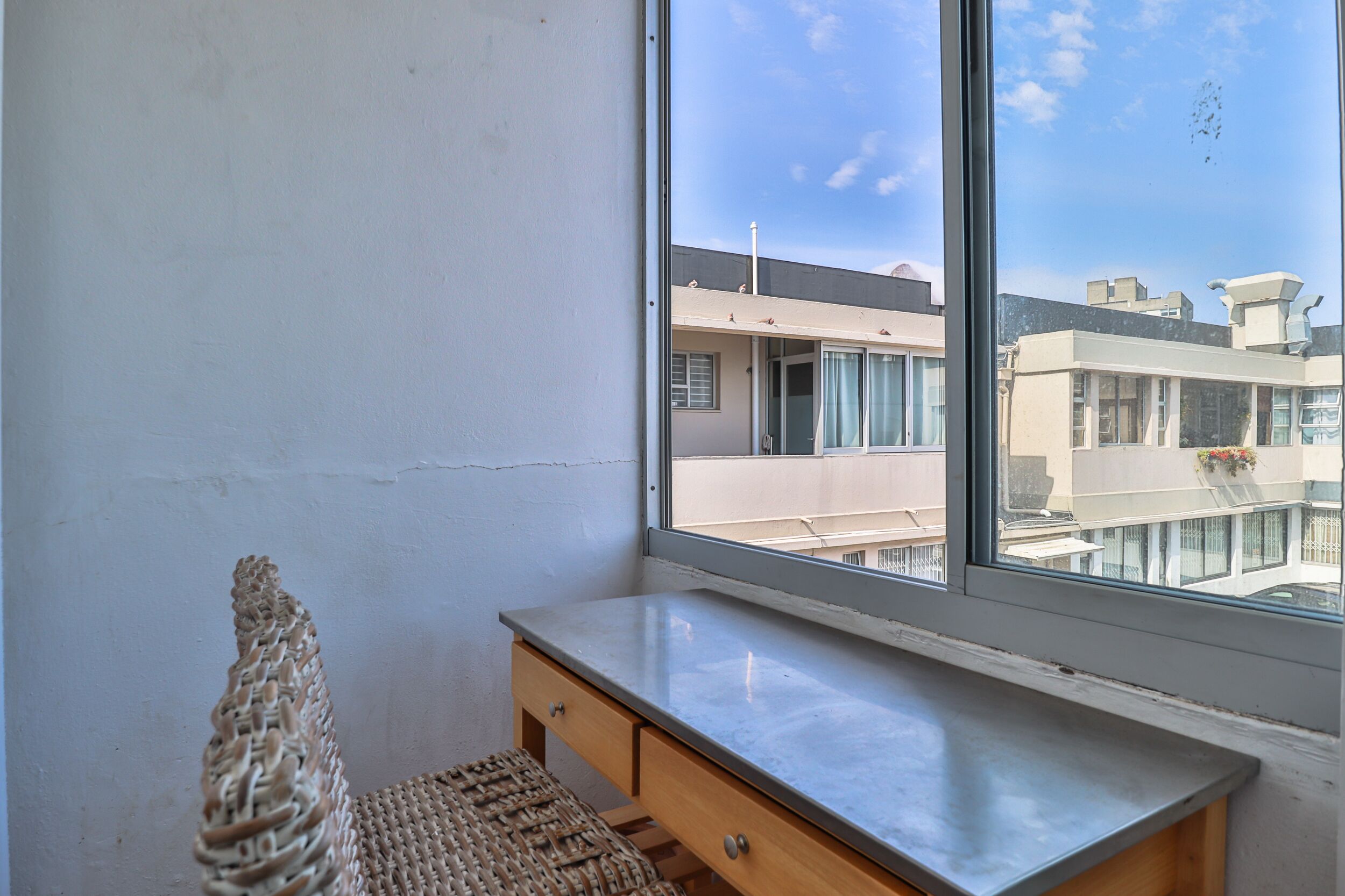 Una habitación con un ventanal grande, un escritorio de madera y una silla de fibras naturales.