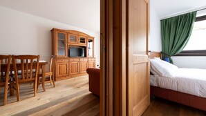 A room with a wooden cabinet, a television, a bed, and a chair. - Italianway - Funivia (Bormio)