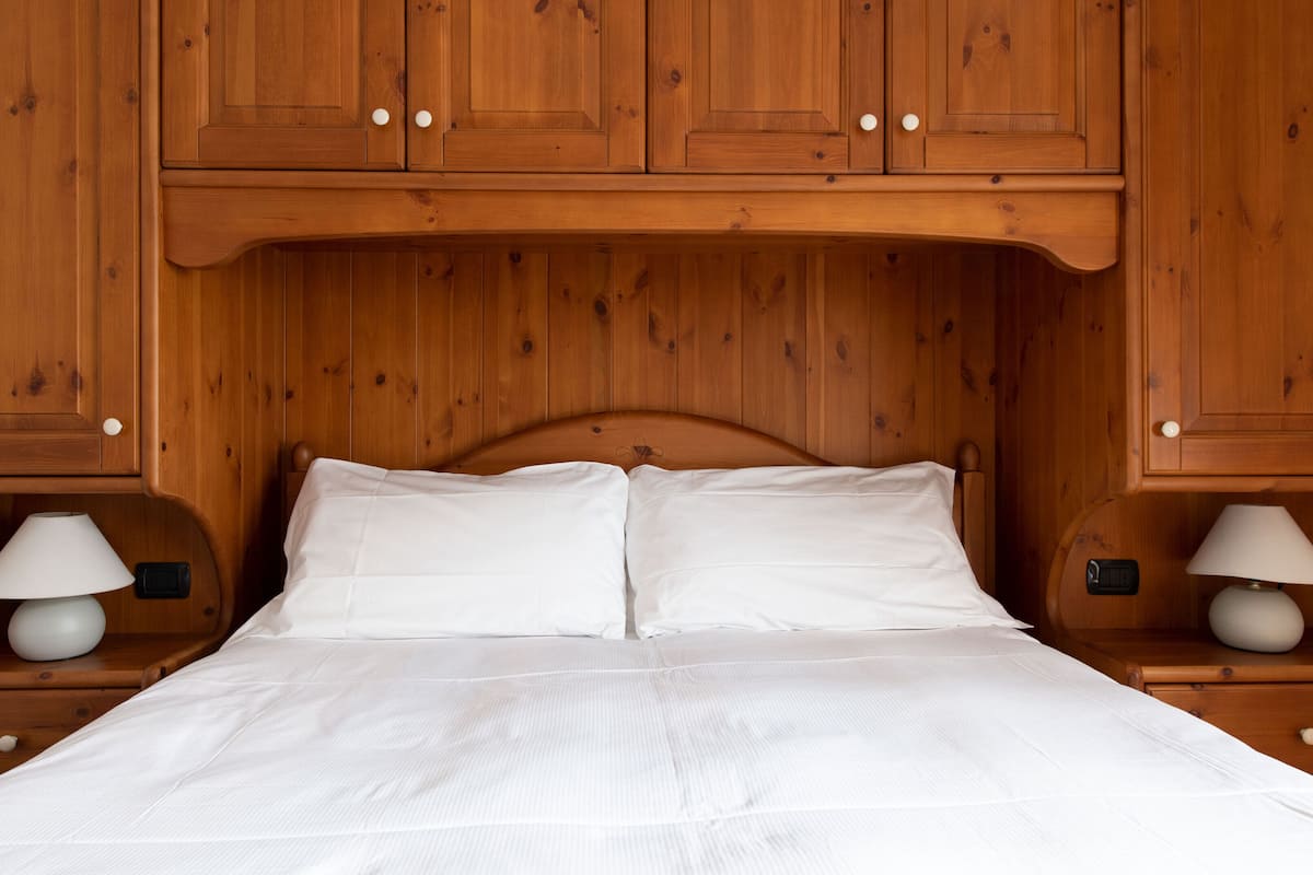 A wooden bed with white linens, flanked by wooden nightstands with lamps, in a room with wooden paneling.