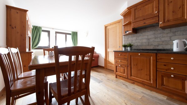 A kitchen with wooden cabinets, a dining table with chairs, and a window with curtains. - Italianway - Funivia (Bormio)