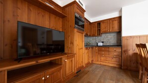 A kitchen with wooden cabinets, a built-in oven, a large flat-screen TV, and a coffee maker. - Italianway - Funivia (Bormio)