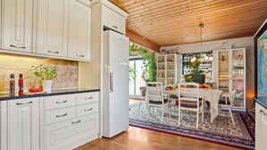Una cocina moderna con muebles blancos, techo de madera y comedor con mesa y sillas.