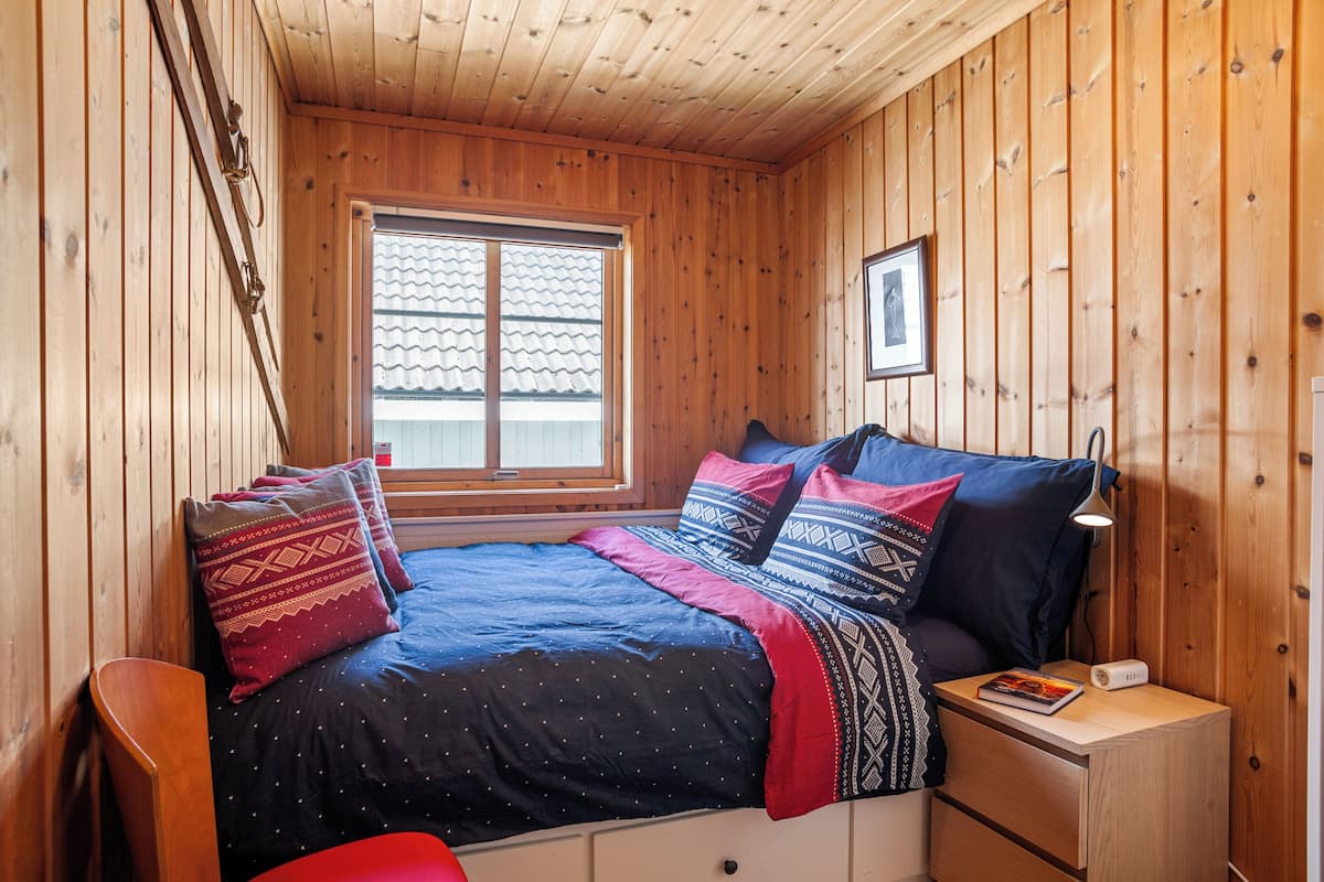A wooden-paneled room with a bed, a nightstand, a chair, and a window.