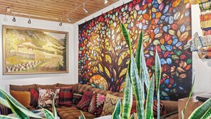 Una sala de estar acogedora con un cuadro grande de un paisaje rural y un mural de un árbol colorido.