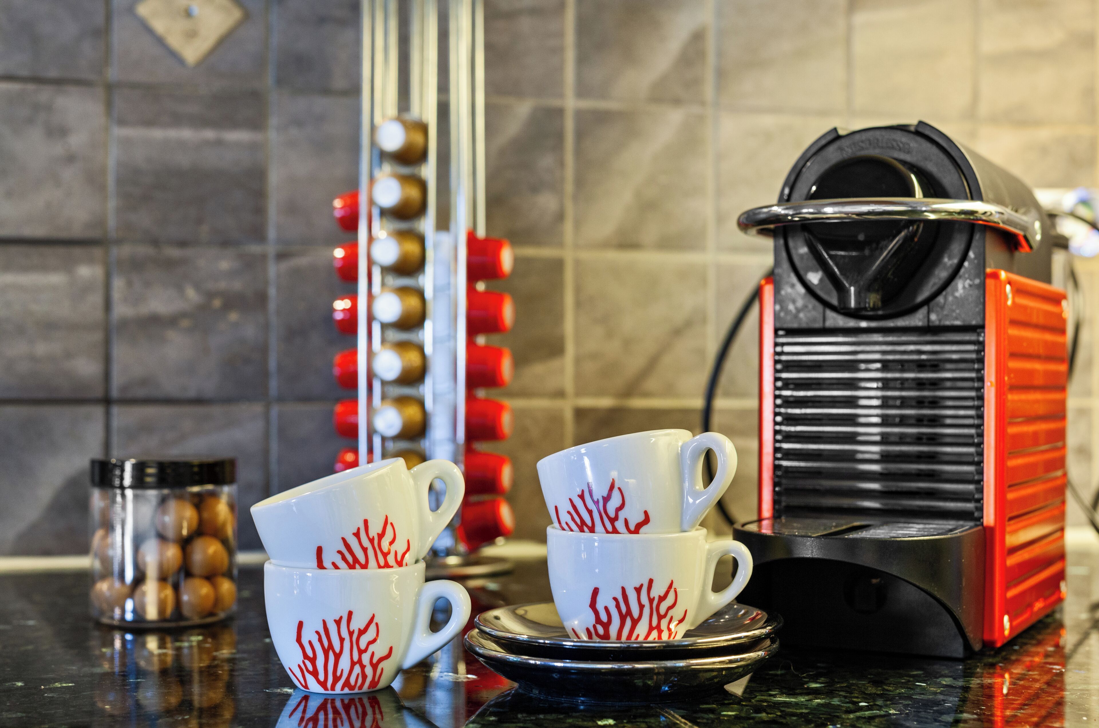 A kitchen with a coffee maker, cups, and a jar of coffee beans.