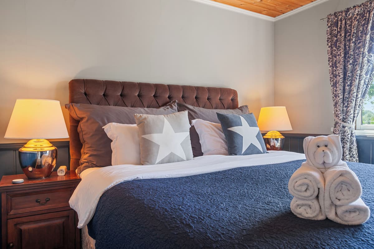 A neatly made bed with a blue blanket, a teddy bear, and star-patterned pillows.